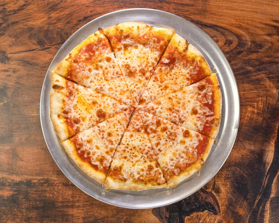 A classic cheese pizza, cut into eight slices, on a metal pan atop a rustic wooden table.