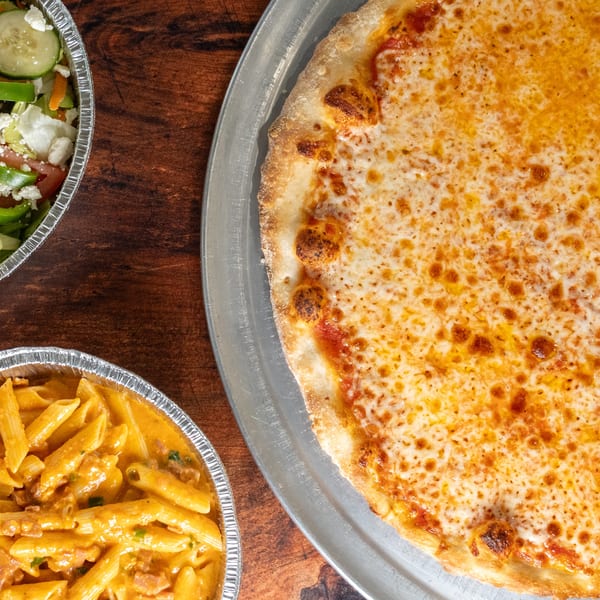 A cheese pizza, a penne pasta dish, and a salad with feta cheese on a wooden table.