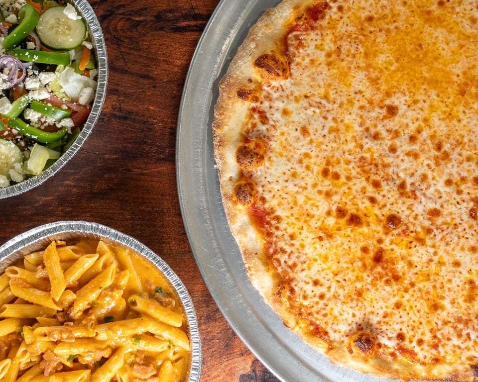 A cheese pizza, a penne pasta dish, and a salad with feta cheese on a wooden table.