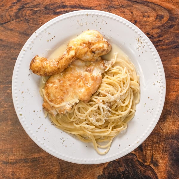 Chicken Francese with spaghetti and parmesan cheese on a white plate.