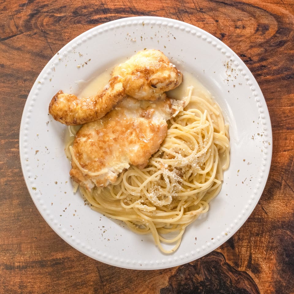 Chicken Francese with spaghetti and parmesan cheese on a white plate.