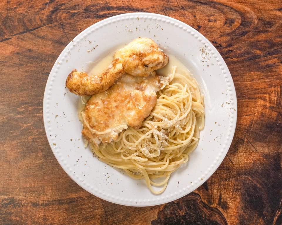 Chicken Francese with spaghetti and parmesan cheese on a white plate.