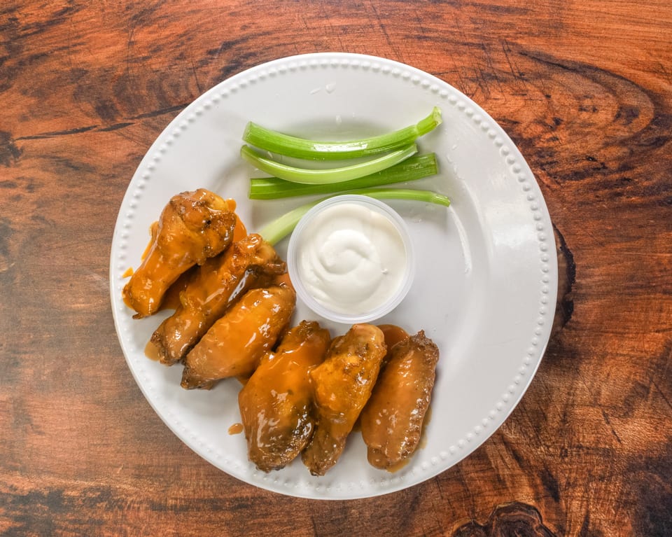 Plate of chicken wings with orange sauce, celery sticks, and a side of ranch dressing.