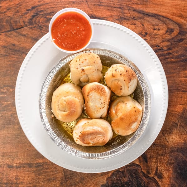 Garlic knots in a foil tin with marinara sauce on a white plate and wooden table.