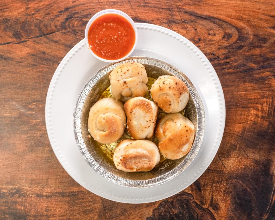 Garlic knots in a foil tin with marinara sauce on a white plate and wooden table.