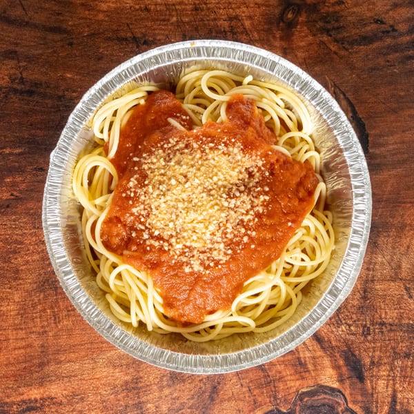 Spaghetti with red sauce and parmesan cheese in a foil take-out container on a wooden table.