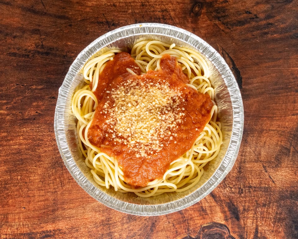 Spaghetti with red sauce and parmesan cheese in a foil take-out container on a wooden table.