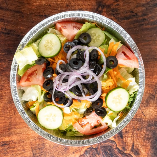 Fresh garden salad with lettuce, tomatoes, cucumbers, black olives, and red onion in a foil container.