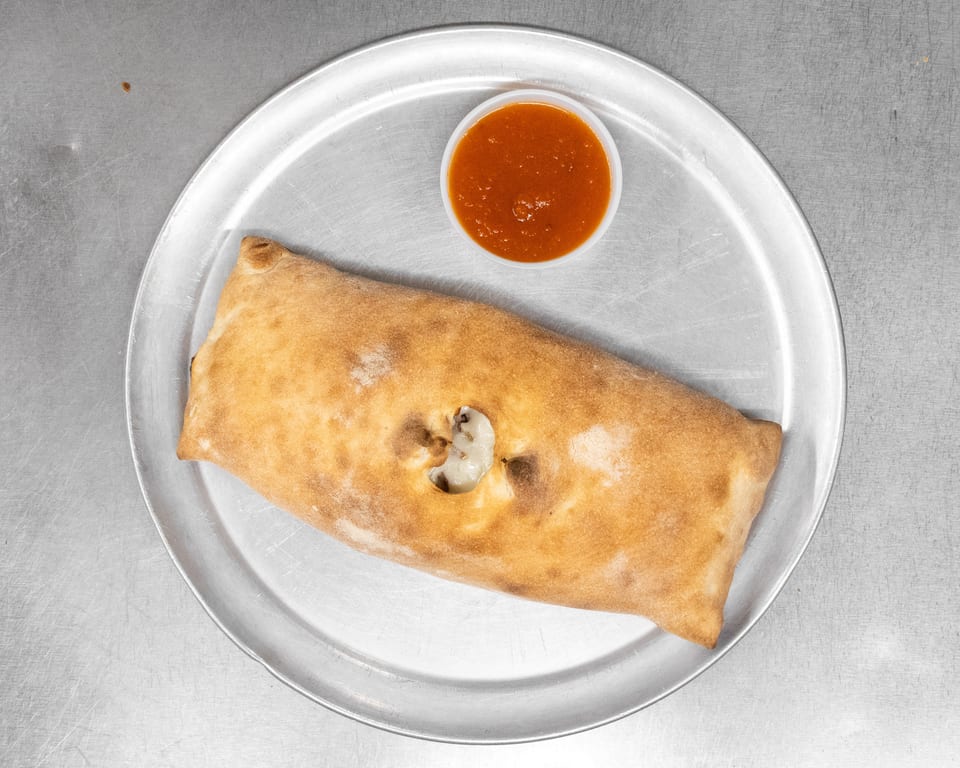 A golden-brown calzone with a small hole revealing cheese, served with a side of marinara sauce.