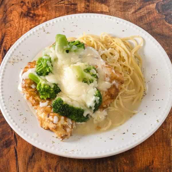 Chicken and broccoli alfredo with spaghetti on a white plate, on a wooden table.
