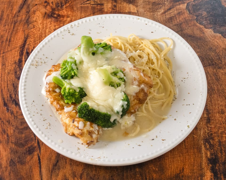 Chicken and broccoli alfredo with spaghetti on a white plate, on a wooden table.
