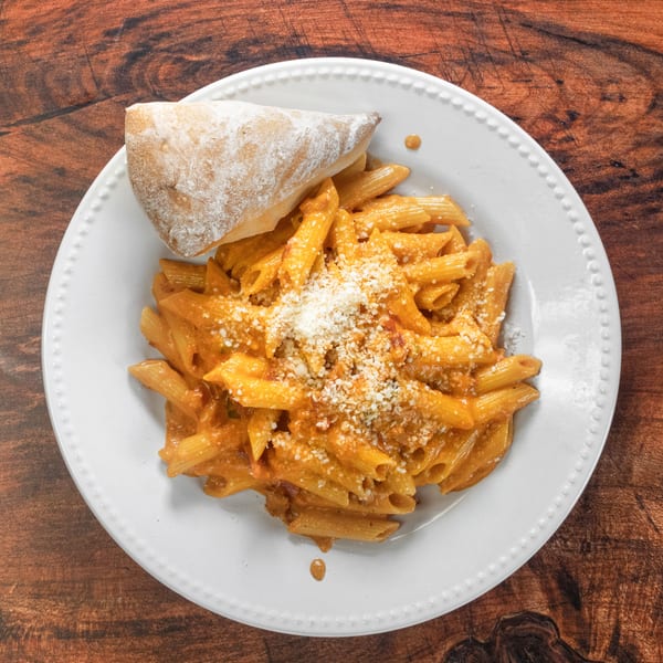 Penne pasta in a creamy tomato sauce, topped with grated cheese and a side of bread.