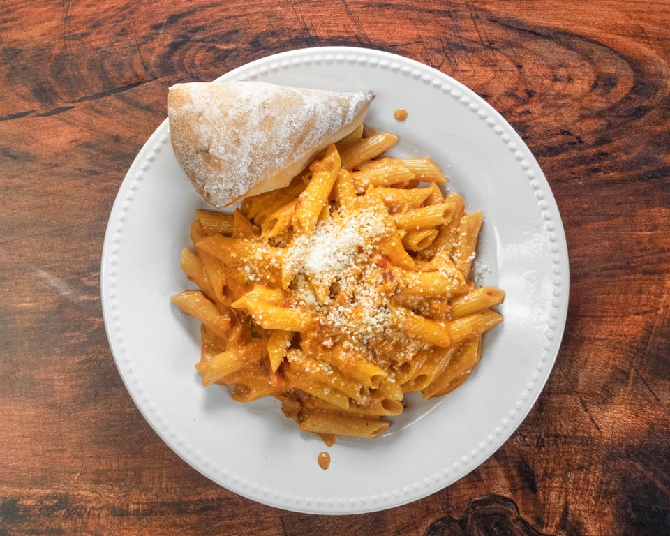 Penne pasta in a creamy tomato sauce, topped with grated cheese and a side of bread.