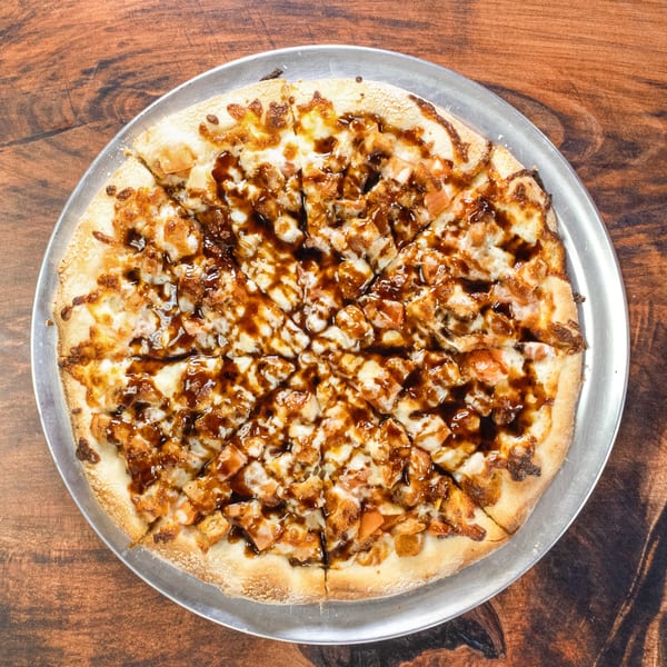 A whole BBQ chicken pizza, cut into slices, on a metal pan atop a wooden table.