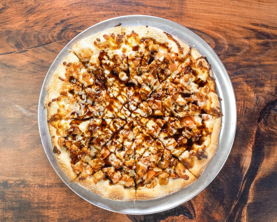 A whole BBQ chicken pizza, cut into slices, on a metal pan atop a wooden table.
