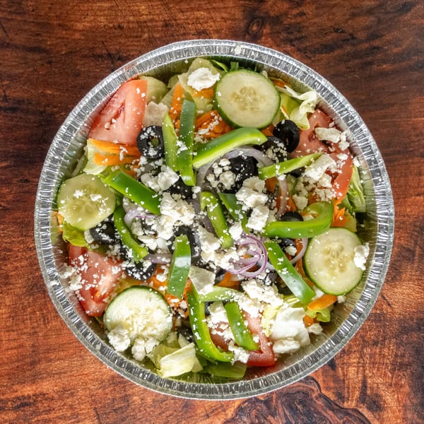 A vibrant salad with lettuce, tomatoes, cucumbers, olives, green peppers, and feta cheese in a foil container.