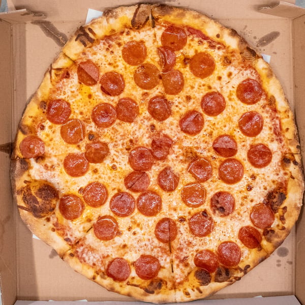 A large, round pepperoni pizza with melted cheese and a golden crust sits in a cardboard box.