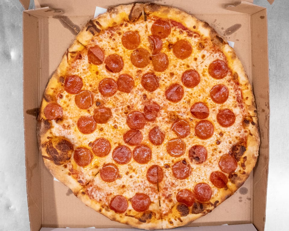 A large, round pepperoni pizza with melted cheese and a golden crust sits in a cardboard box.