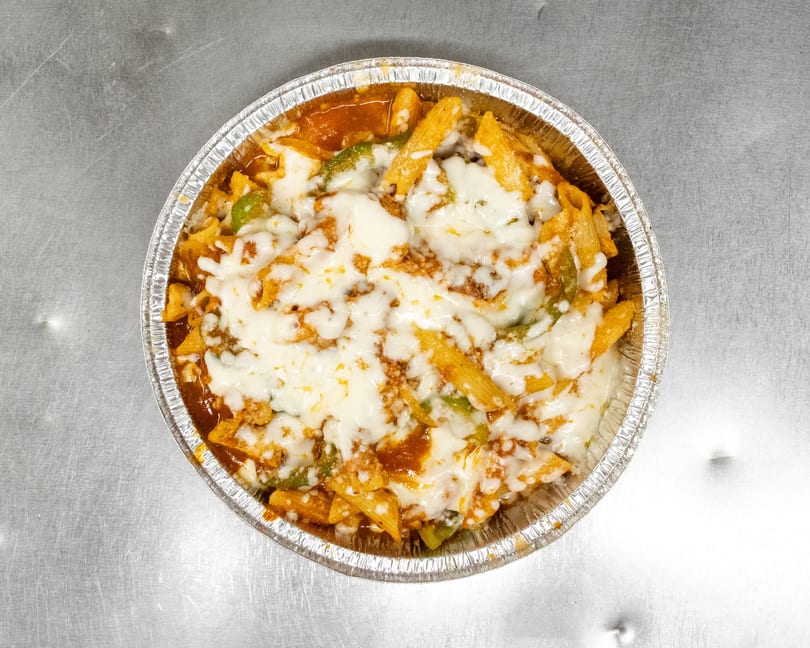 Baked penne pasta with melted mozzarella cheese, tomato sauce, and green peppers in a foil pan.