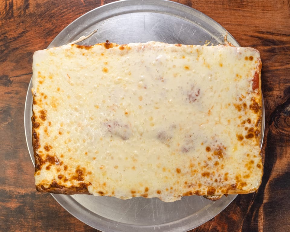 A rectangular cheese pizza with a thick crust and bubbly, golden-brown cheese on a metal tray.