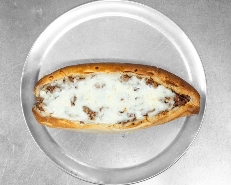 A cheesy steak sub sandwich on a metal tray, viewed from directly above.