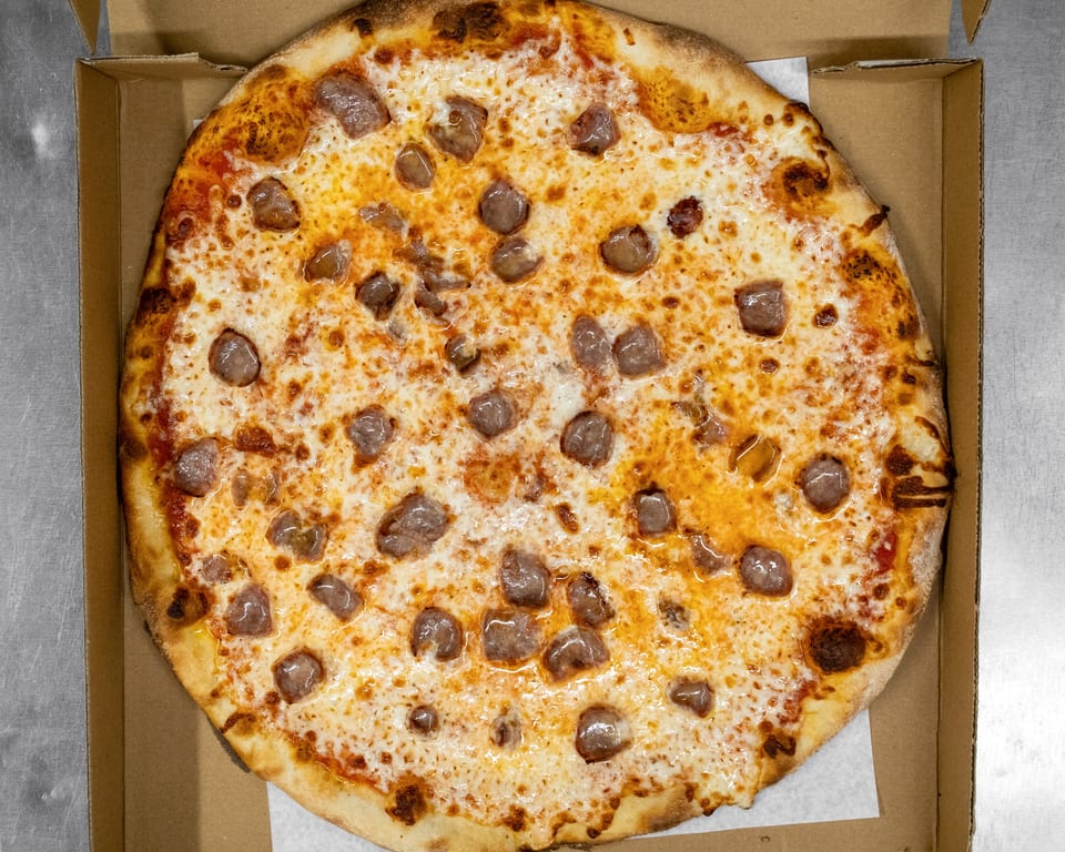 A whole sausage pizza with melted cheese and red sauce in a cardboard delivery box.