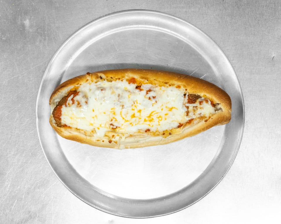 A meatball sub with melted mozzarella cheese and marinara sauce on a metal pizza pan.