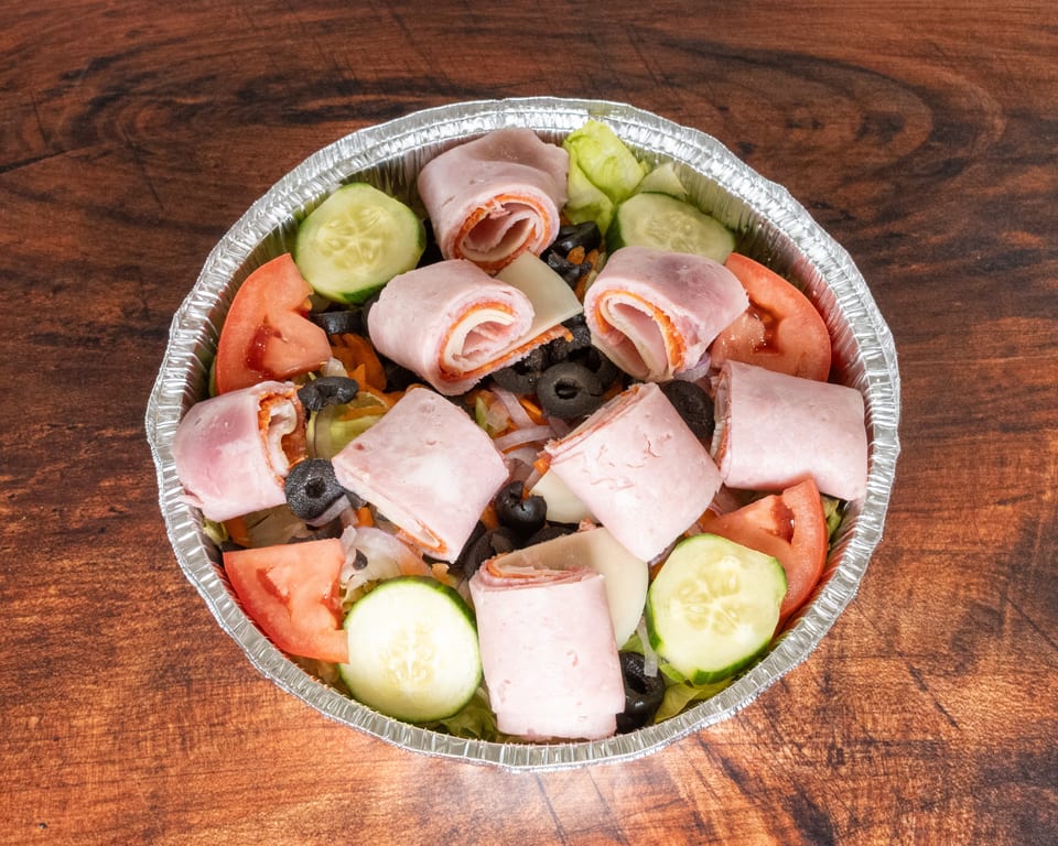 Antipasto salad in a foil container with ham and cheese rolls, tomatoes, cucumbers, and olives.